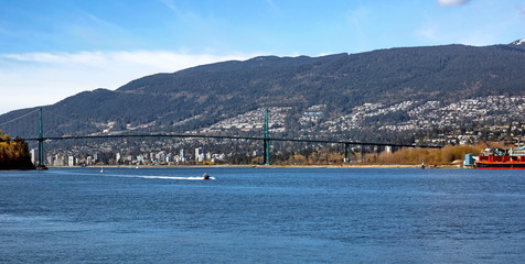 Lion Gate Bridge and City by the Sea, a motor boat going under the bridge on the background of mountain landscapes