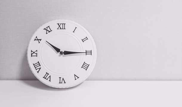 Closeup white clock for decorate show a quarter past ten o'clock or 10:15 a.m. on white wood desk and wallpaper textured background in black and white tone with copy space
