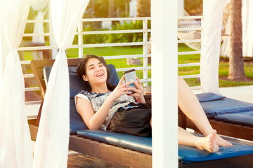 Teen girl using smartphone while relaxing on lounger at resort