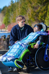 Fototapeta na wymiar Disabled boy in wheelchair talking with father at lakeside park