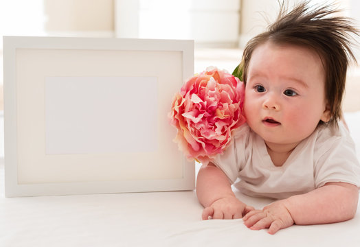 Happy baby boy with photo frame and flower