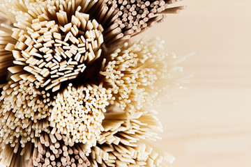 Cross-section of different bundles of raw noodles close up on soft beige wooden board, top view.