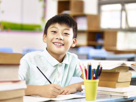 asian elementary schoolboy doing homework in classroom