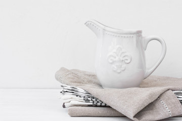 White vintage pitcher on a stack of linen towels, styled image with copyspace for product marketing, social media, banner, header