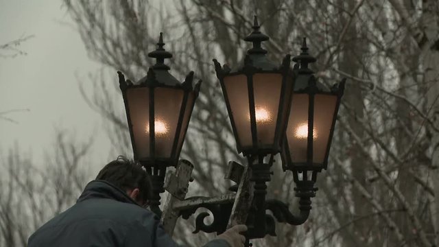 A city service worker changing lamps on a lamp post