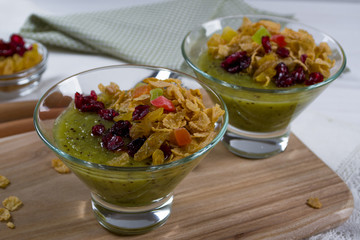 Healthy breakfast, summer dessert with smoothie kiwi, corn flakes and dried fruits in a glassware on white background.