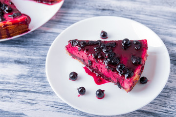 Piece of cheesecake on white plate  with currant on colored wooden background