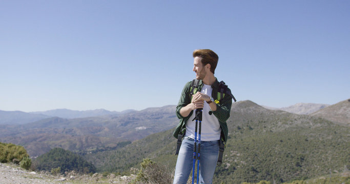 Young man with backpack standing with trekking poles on mountain plat and looking away on beautiful background. 