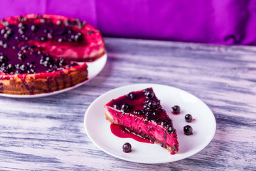 Piece of cheesecake on white plate  with currant on colored wooden background