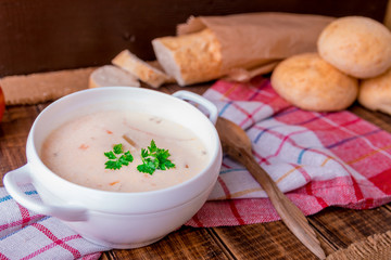 Cream soup in white bowl with wood spoon near bread on wooden background. Rustic style.