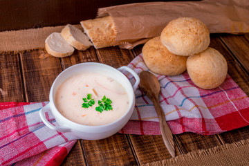 Cream soup in white bowl with wood spoon near bread on wooden background. Rustic style.
