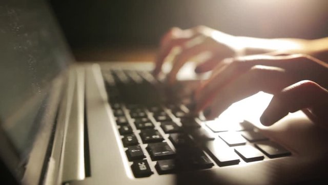 Dolly shot of a woman's hands typing on a laptop keyboard.