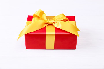 Gift box with yellow bow. Present wrapped with ribbon. Christmas or birthday red package. On white wooden table.
