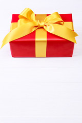 Gift box with yellow bow. Present wrapped with ribbon. Christmas or birthday red package. On white wooden table.