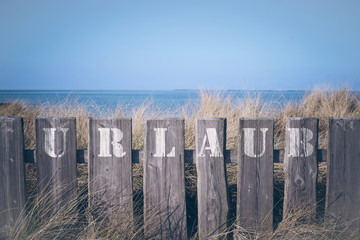 closeup of word Urlaub (German for vacation) written on wooden fence with in front of grass covered...