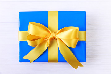 Gift box with yellow bow. Present wrapped with ribbon. Christmas or birthday blue package. On white wooden table.