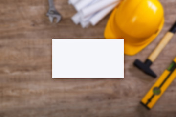 Business card mockup. Adjustable wrench, hammer and building level. Paper plans and helmet. Wood rustic background.