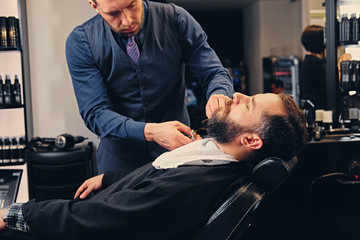 Stylish barber grooming a man's beard in a saloon.