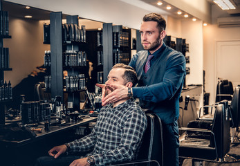 Hairdresser doing haircut to a bearded man in a barbershop.