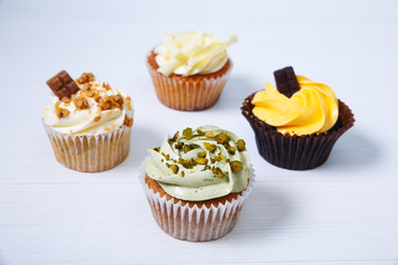 Cupcakes with buttercream. Sweet cake with pistachio cream and small chocolate bar. Dessert on white wooden background.