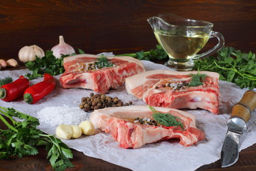 Chunks of fresh chilled pork lie on parchment paper among spices and greens.