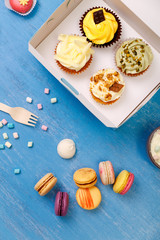 Fototapeta premium Cupcakes and macaroons. Sweet dessert in delivery box. Mug with whipped cream and marshmallows. Almond macaron cookies.