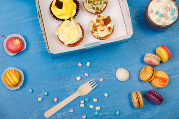 Cupcakes and macaroons. Sweet dessert in delivery box. Mug with whipped cream and marshmallows. Almond macaron cookies.