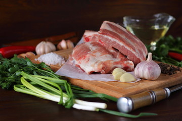 Ribs of raw pork lie on a cutting board among greenery and spices.