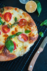 Top view of Pizza with tomatoes and mozarella on a wire rack on a black stone background