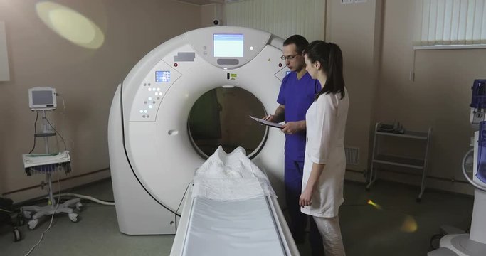 4K Two doctors discuss the patient's medical history in the CT scan room in a new modern cancer treatment hospital.