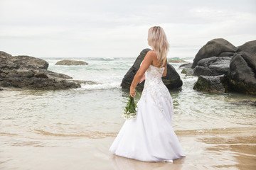 Fototapeta na wymiar Beautiful bride at the beach with a flower bouquet.
