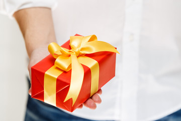 Male hand holding a gift box. Present wrapped with ribbon and bow. Christmas or birthday red package. Man in white shirt.