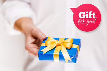 Male hand holding a gift box. Present wrapped with ribbon and bow. Gift for you speech bubble. Man in white shirt.
