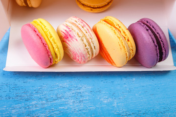 Macaroon cakes. Colored almond macaron cookies. Delivery box. Different flavors. On blue wooden rustic background.