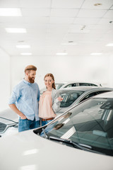 Fototapeta na wymiar Happy couple choosing car in dealership salon, woman pointing on car