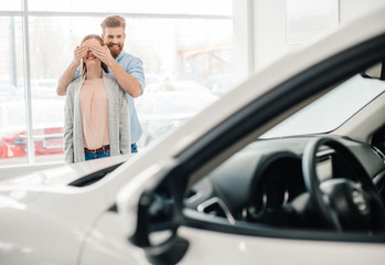 Man closing woman's eyes to make a surprise in dealership salon