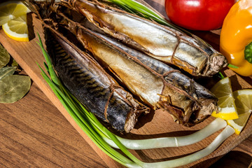 Smoked fish mackerel on wooden cutting board on background of vegetables (pepper, tomato, green onions)