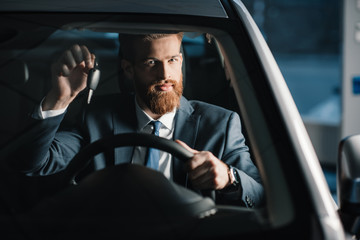Bearded young businessman holding key while sitting in new car