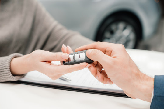 Close-up partial view of dealer giving car key to new owner