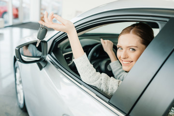 Happy young woman holding key while sitting in new car