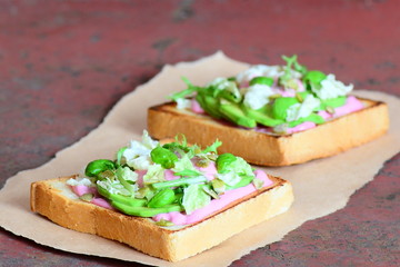 Sliced avocado, pumpkin seeds, lettuce, basil and beetroot sauce on a white toast bread. Open sandwiches on a paper and on a vintage metal background. Delicious and healthy toast meal. Closeup