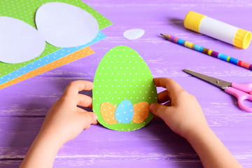 Small child holds a Easter paper card in hands. Child made Easter greeting card in egg shape....