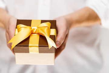 Male hands holding a gift box. Present wrapped with ribbon and bow. Christmas or birthday package. Man in white shirt.