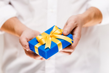 Male hands holding a gift box. Present wrapped with ribbon and bow. Christmas or birthday blue package. Man in white shirt.