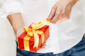 Male hands holding a gift box. Present wrapped with ribbon and bow. Christmas or birthday red package. Man in white shirt pulls the ribbon.