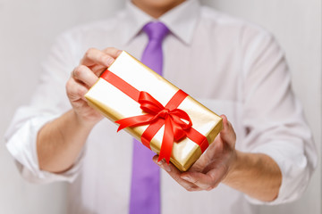 Male hands holding a gift box. Present wrapped with ribbon and bow. Christmas or birthday package. Man in white shirt and necktie.
