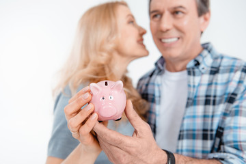 Front view of happy couple holding piggy bank on white