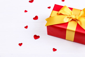 Gift box with red satin hearts. Present wrapped with yellow ribbon. Christmas or birthday package. On white wooden table.