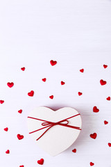 Gift box with hearts. Heart-shaped present wrapped with ribbon and bow. Valentines day love package. On white wooden table.