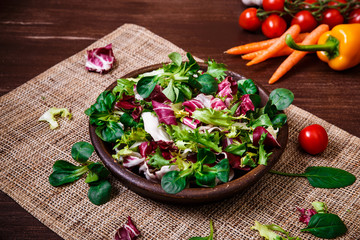 Provence salad. Leaves of endive or chicory, lamb and rose salad. Cherry tomatoes, pepper and carrot. Raw vegetables. On wooden table.